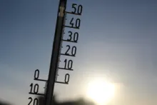 Thermometer vor einem blauen Himmel und Sonne