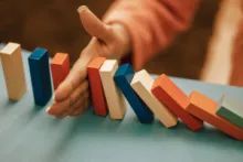 Eine Hand, die Dominosteine vor dem Umfallen stoppt