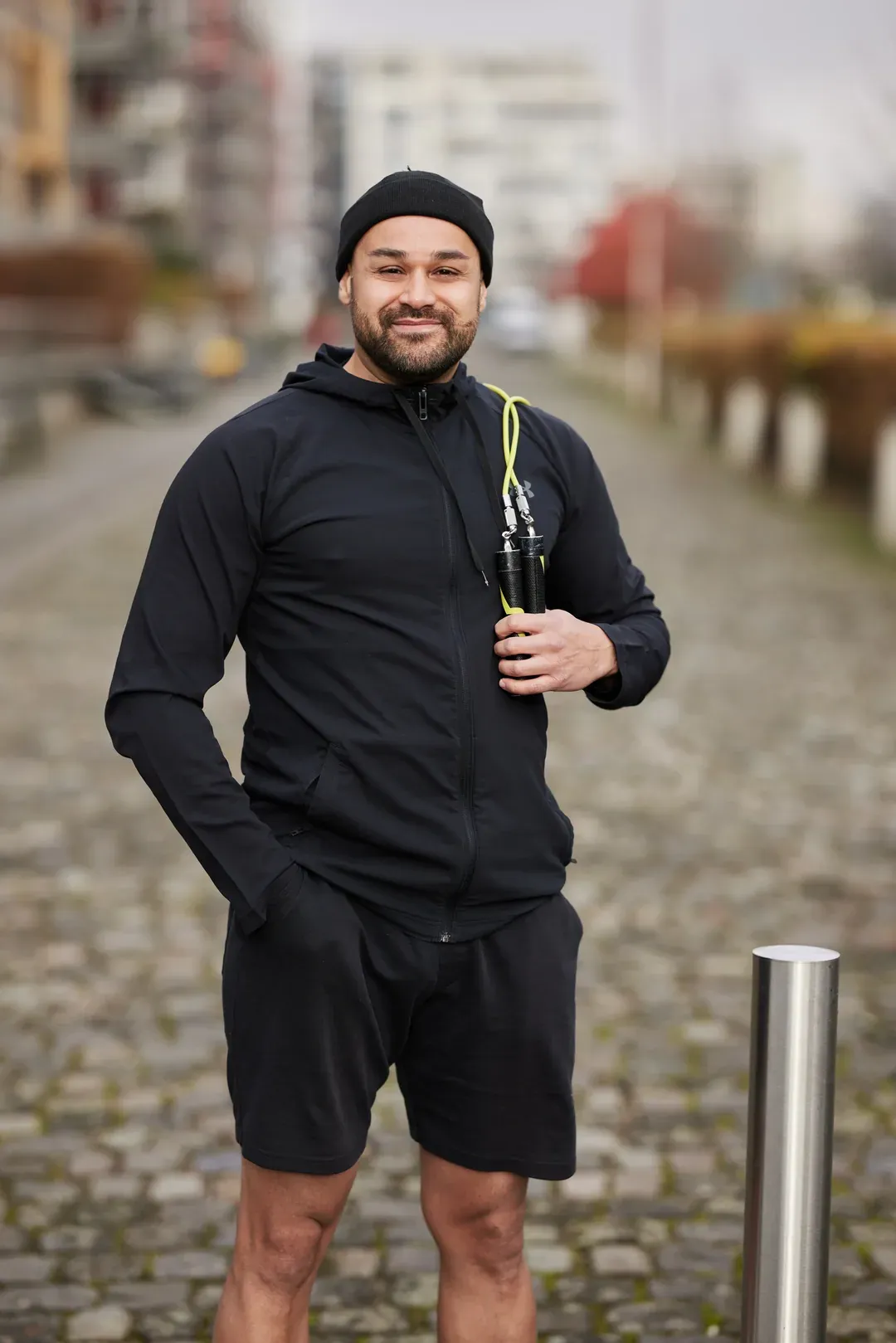 Mann in schwarzer Sportkleidung steht auf einem gepflasterten Weg im Freien.