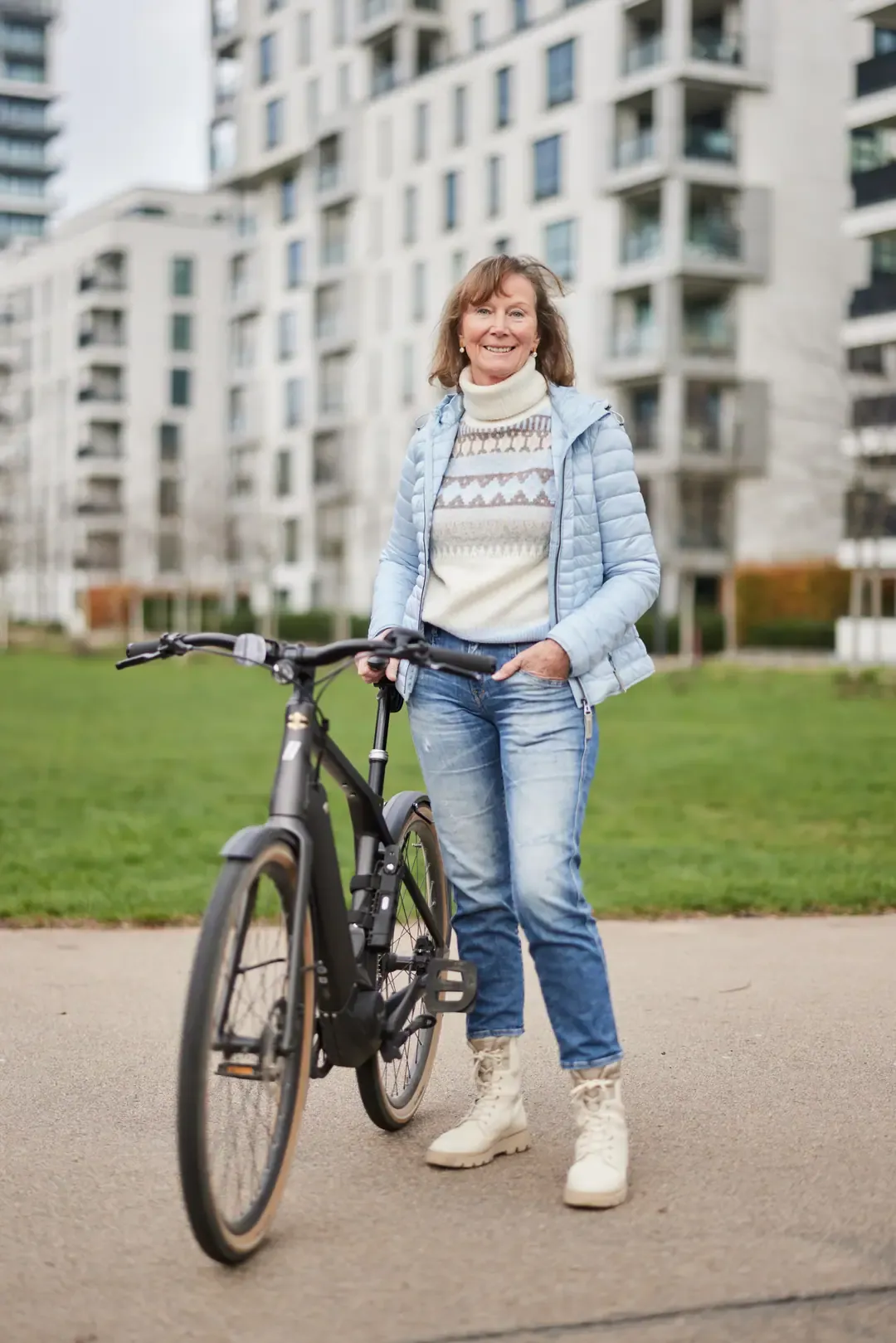 Frau steht mit einem Fahrrad vor der Grünfläche einer Wohnanlage.